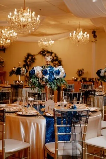 Blue and white reception room setup with chandeliers, round tables, and gold chairs at Nencini Ballroom