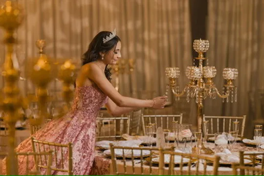 Quinceañera in a pink dress adjusting a candelabra beside gold reception decor at Nencini Ballroom