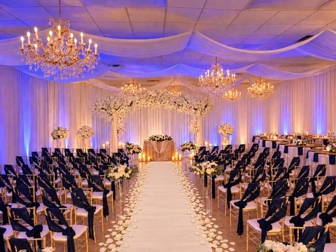 Navy chairs and a white wedding aisle facing the floral ceremony backdrop at Nencini Ballroom